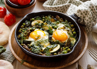 Green shakshuka with green vegetables and fried eggs in cast iron skillet, close up view