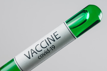Vacuum tube with a sample of Covid-19 vaccine of green color in the hand with a medical glove on a white background