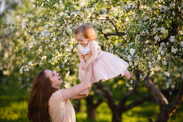 Family time. Mother and little daughter play in blooming apple garden. Mom loves her child. Spring story. Toddler girl sits on little chair in apple garden. Happy family in beautiful spring day