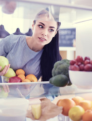 Smiling woman taking a fresh fruit out of the fridge, healthy food concept