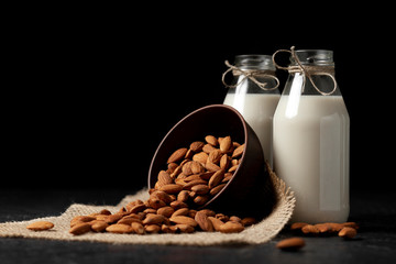 lactose-free almond milk in bottles with nuts on a dark black table, vegetarian milk drink, healthy milk product