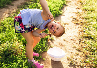 Beautiful playful fun kid girl enjoying green grass summer sunny day background in fashion sunglasses and hat. Closeup