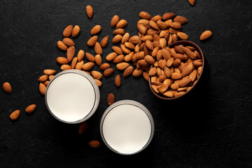 Obraz na płótnie Canvas sprinkled almonds with glasses of milk on a black background, vegetarian milk without sugar and lactose, top view