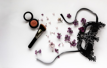 A composition of a masquerade black mask, spring flowers and tassels on a white background. Purple...