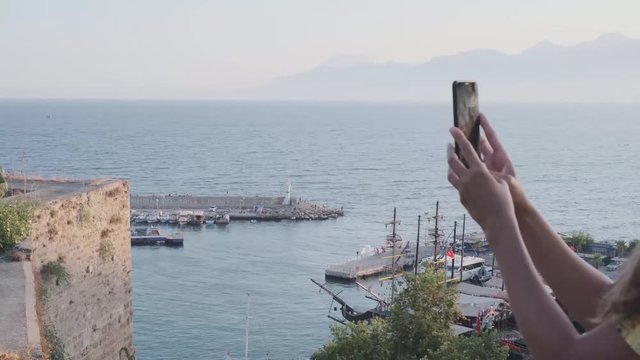 Young woman makes photo on smartphone. Panorama of old Antalya, Kaleici harbor, view of the sea and mountains in the fog