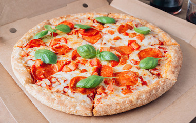 Pizza box delivery concept. Open box with hot tasty italian sliced pepperoni pizza with basil. Selective focus
