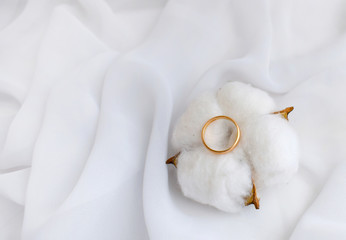 Elegant wedding concept. Golden ring with cotton flower pillow on white silk background. Feminine still life composition. Minimalist style. Copyspace.