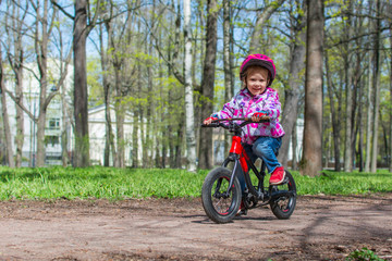 Little cute girl is riding a bicycle in the spring park. Child learning to drive a bicycle on a path outside.