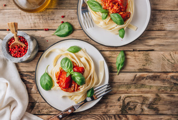 Pasta Tagliatelle Bolognese with meat tomato sauce and fresh basil leaves on white plate. Light gray table. Top view