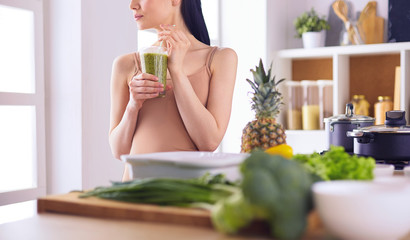 Young woman with glass of tasty healthy smoothie at table in kitchen