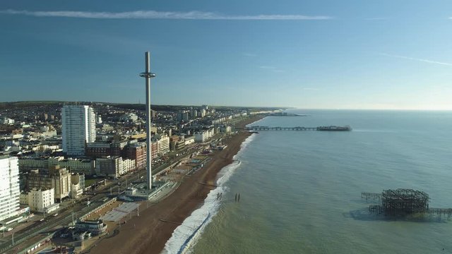 Brighton West Pier, British Airways i360 viewing pod at the top of the tower and Brighton Palace Pier with calm sea, waves crashing and blue sky