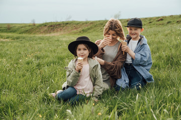 Fototapeta premium Happy family, mom daughter and son in organic clothes, walk in the field and eat ice cream. The concept of a healthy lifestyle, happiness and joy