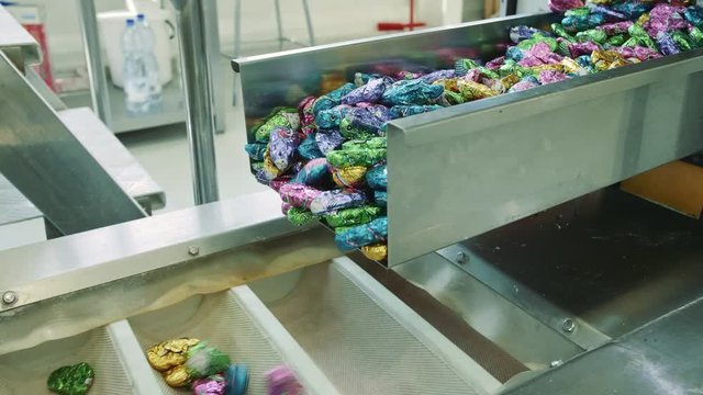 Candy factory. Sweets spilling from conveyor. Bunch of wrapped candies falling from conveyor on packing containers in confectionery factory.