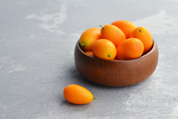 Kumquat fruits in wooden bowl on light stony background. Healthy vegetarian food. Copy space.