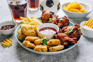 Table fof tasty snacks for beer prepared for watching sports on TV. Chicken. Chicken wings, chicken nuggets, french fries, chips, various sauces and lemonade. Light gray background. Selective focus