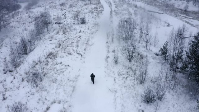 alone one man men walks through the snow white desert  somewhere in russia Siberia stalker in hood aerial drone view with snowflakes