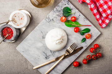 Salad with Italian burrata cheese, arugula, spinach, cherry tomatoes and olive oil served on marble plate. Top view. Light gray concrete background