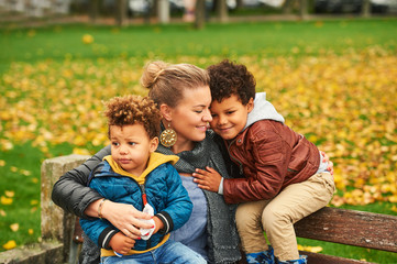 Outdoor portrait of happy young mother with two lovely sons, family enjoying nice autumn day in...
