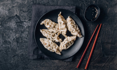 Asian dumplings with soy sauce and sesame seeds on black background. Black table setting. Copy space