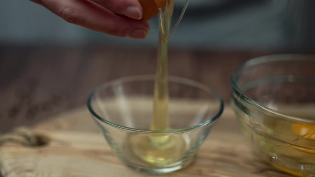 Close-up of cracking an egg and separating white from yellow in a glass bowl on a wooden table