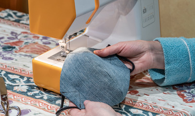 woman making a medical face mask with a sewing machine during the crown virus pandemic. Homemade...
