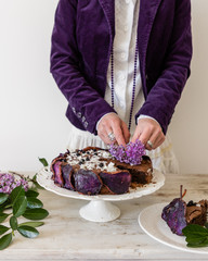 A woman dressed in Vintage Purple clothing decorates a Purple Flower Spring Cake 