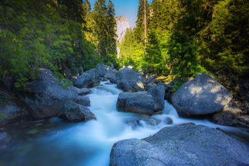 Gushing waters of the swirling Tuolumne river with huge river rocks in Yosemite Park, California.