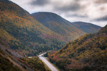 Fototapeta premium Autumn colors of the Cape Breton as the sun rays fall on the valley. Fall foliage of the mountains with multi colored deciduous trees, Cabot Trail, Cape Breton Nova Scotia 