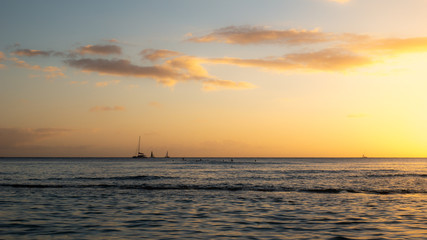 Fototapeta na wymiar Warm sunset on the ocean with sailing boats located on the horizon, shot at Waikiki beach, Honolulu, Hawaii, USA 