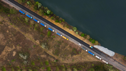 Truck logistic aerial. Manyblue trucks on the highway intersection road between field and lake....