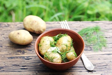 Young boiled potatoes with butter and dill on a wooden background of an old tree. country style. Organic food. copy space