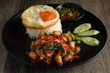 thai food background of spicy thai style stir-fried chicken meat with chilli, basil leaf and garlic served with fried egg topping on rice with chilli fish sauce and cucumber, Thai phat kaphrao rice