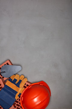 Stack of bricks with masonry trowel, construction hard hat, gloves on gray concrete background. Top view. Construction concept.