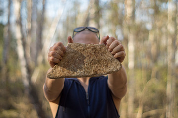 A man holds a stone in his hand, on a blurred background of nature.