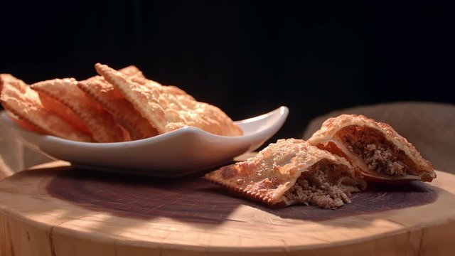 Fried pastry on a plate and a meat pastry cut in half on the wooden board