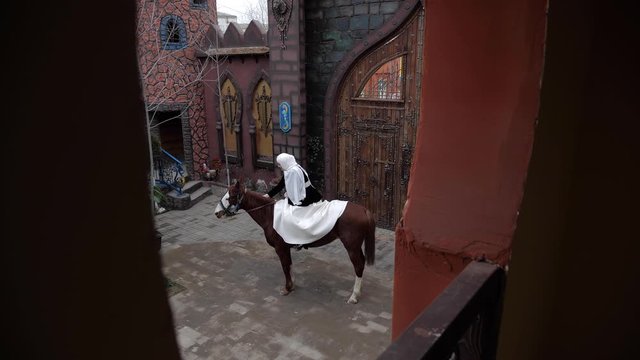 woman in white hijab and long skirt strokes chestnut horse neck near wooden gate view from restaurant terrace slow motion
