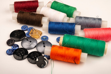 Several reels of multicolored sewing thread and multicolored buttons of different sizes on a white background. Close up.