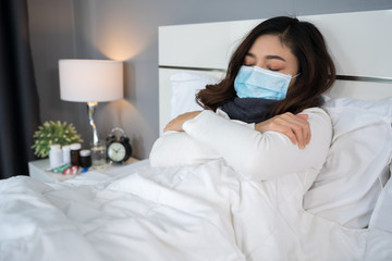 sick woman in medical mask feeling cold and suffering from virus disease and fever in bed,...