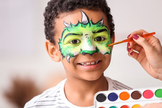 Woman painting face of African-American boy at home