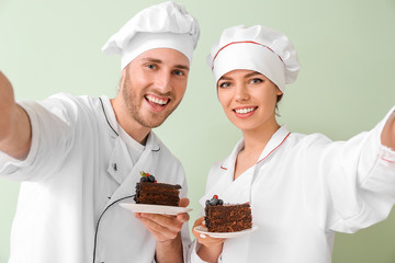 Young confectioners with tasty dessert taking selfie on color background