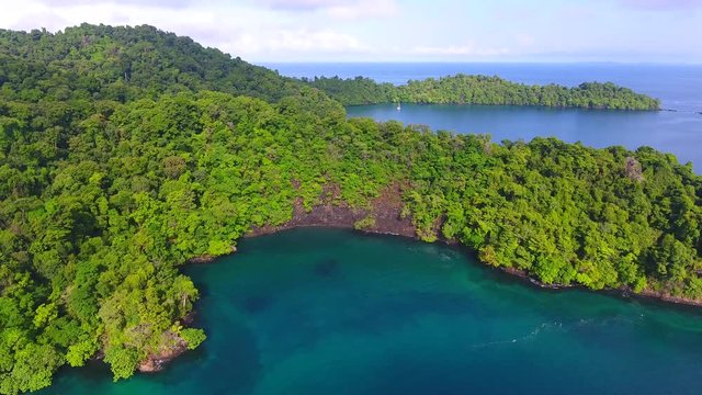 Sideways Flying Aerial View of Anchored Sailboat Near Brincanco Island (Coiba Park)  Blue Lagoons with Dense Jungle Trees and Rock Cliff Shore
