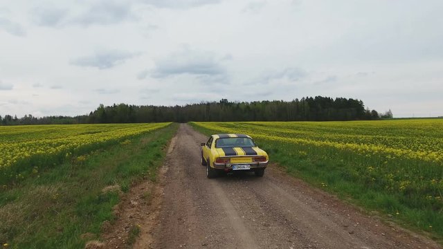 Yellow With Black Stripes Classic Ford Consul Rides On A Gravel Road. 4K Aerial Footage