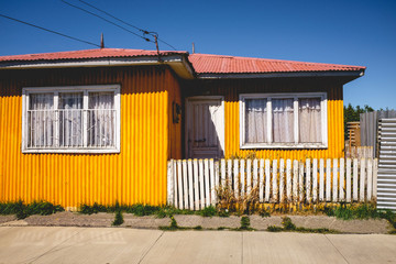 Colorful yellow house with white fence in the streets of Puerto Natales in a sunny day with blue sky