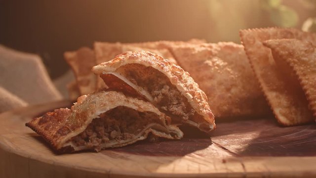 Several fried pasties on a wooden board and a meat pastry cut in half