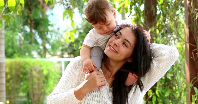 Cute mother and baby son caring and loving relationship. Casual infant sitting on mom shoulders