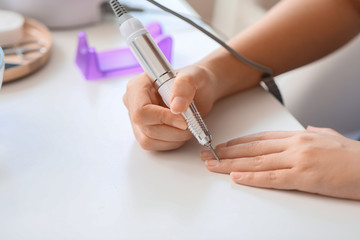 Manicure master working with modern milling cutter in beauty salon, closeup