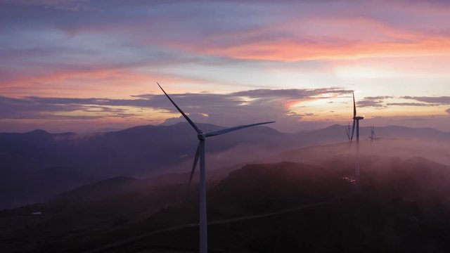 Incredible image of a drone flying in fog near a wind turbine during an extraordinary colorful sunset in Sicily Italy.
