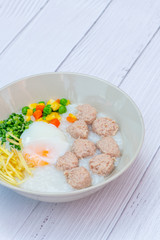 Delicious Thai Hong Kong Style Congee mixed with pork, meat, and Soft-boiled eggs in the round bowl on the white wood background. Thai, Hong Kong breakfast.