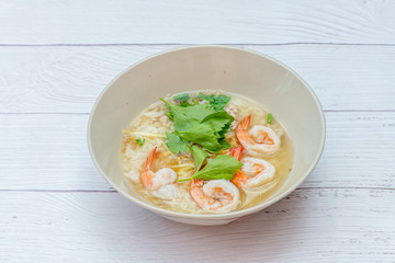 Thai rice soup with shrimp on bowl with white wood background