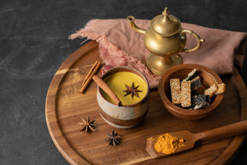 Golden milk made of turmeric and spices in a cup on a wooden tray with sweets. Anti-inflammatory, healthy, Indian drink
